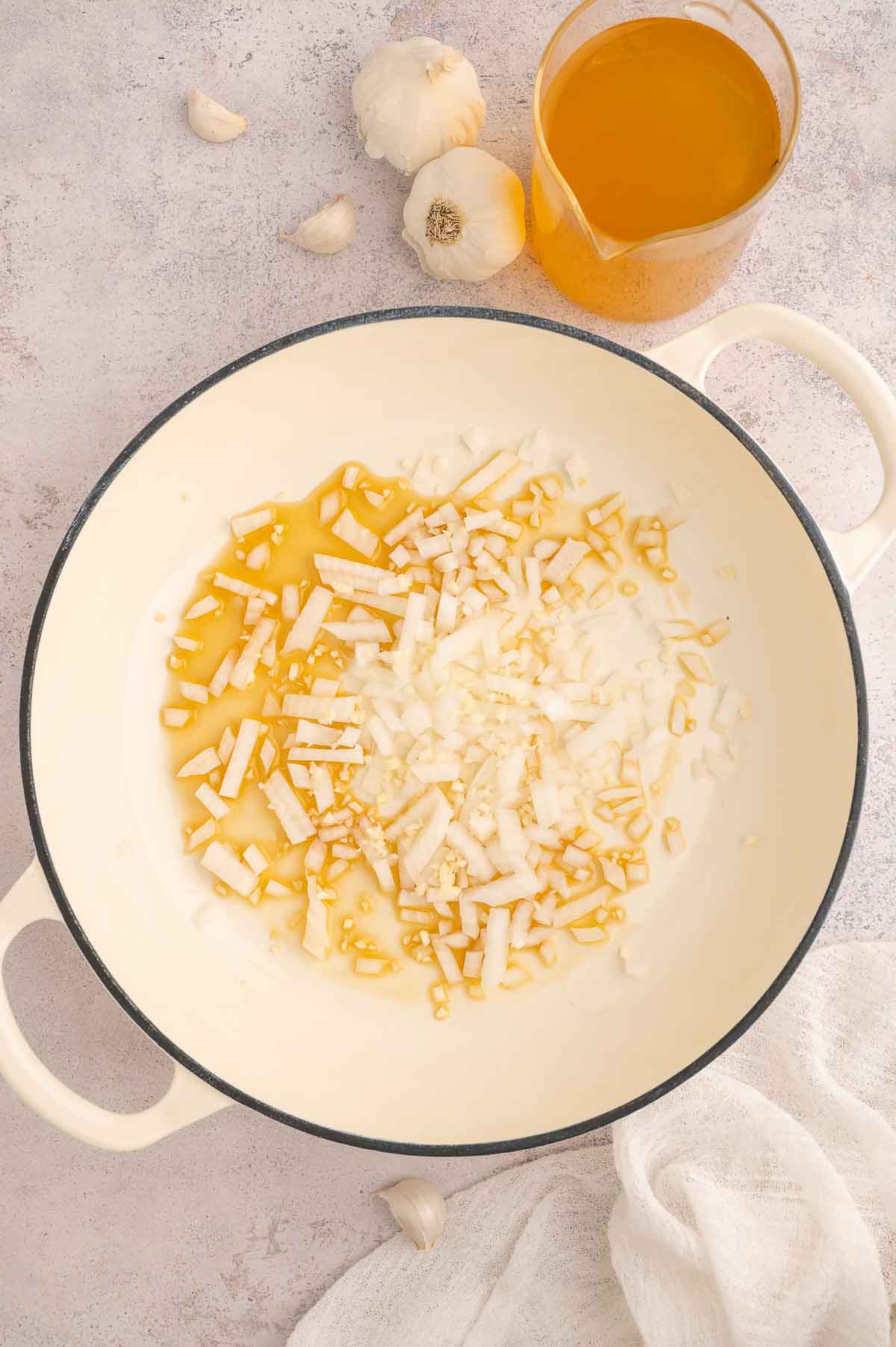 Chopped onion and garlic sautéing in sesame oil in a cream-colored Dutch oven.