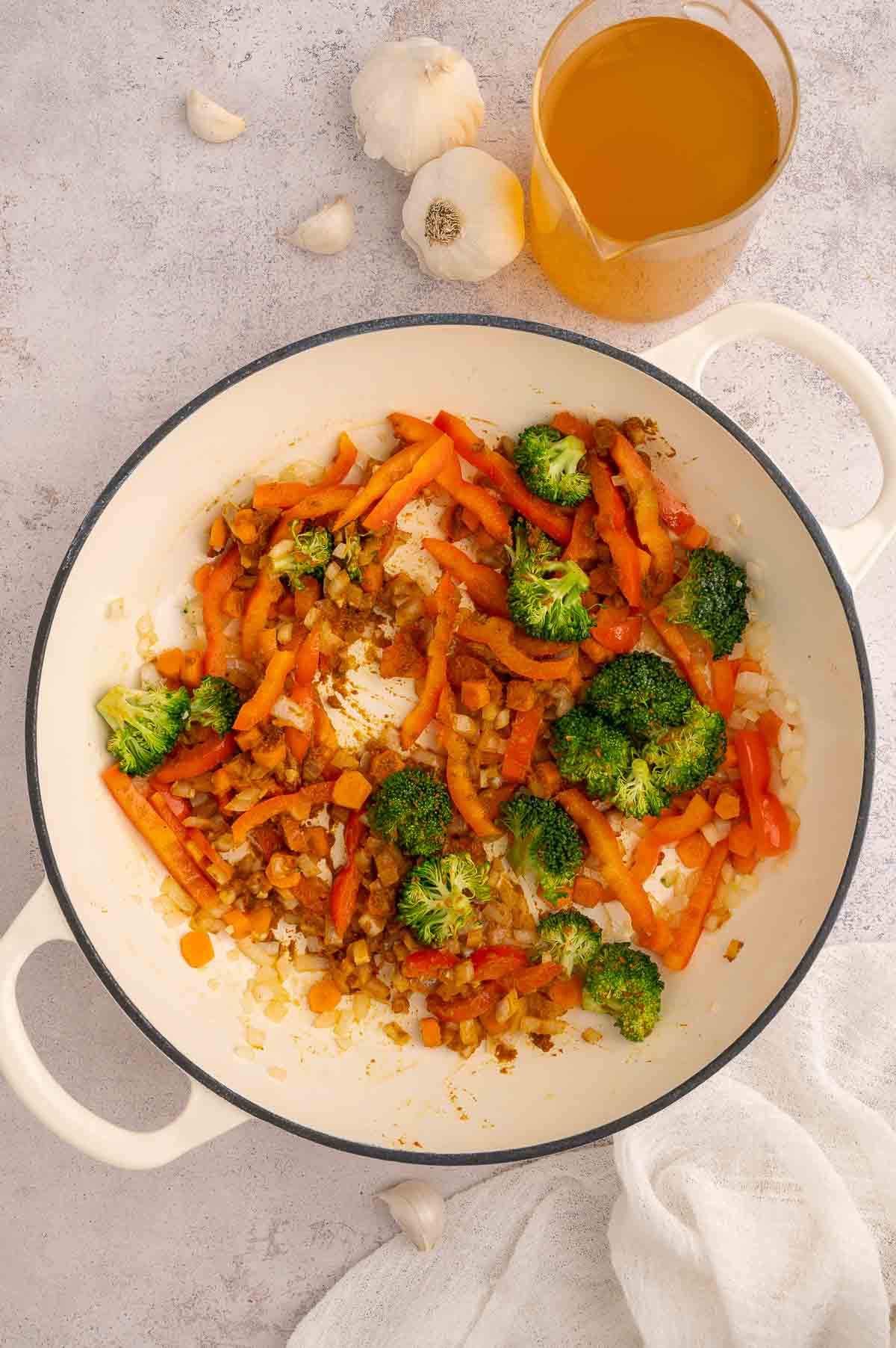 Sautéed carrots, broccoli, red pepper, and curry paste cooking down in a pot.