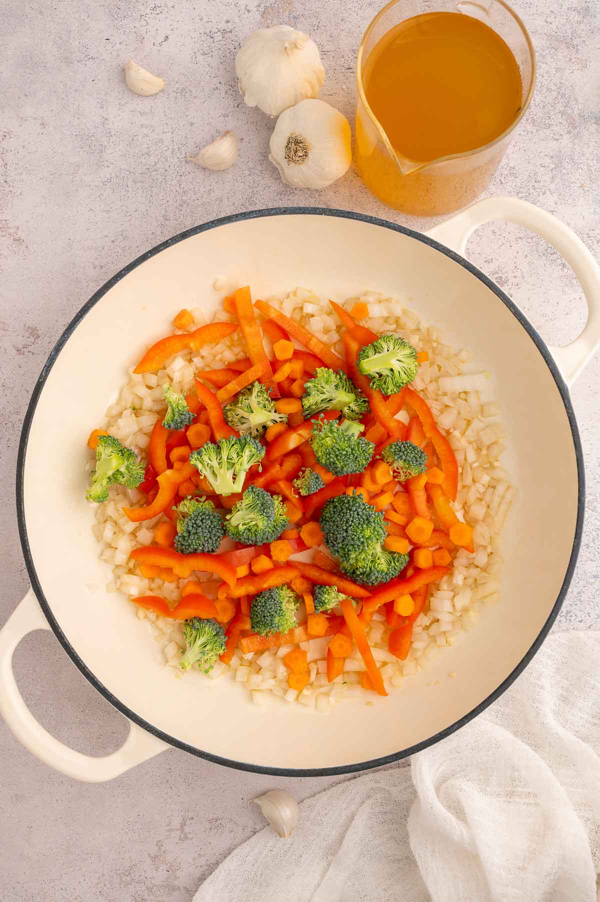 Raw carrots, broccoli, and red bell pepper added to onion base in Dutch oven.