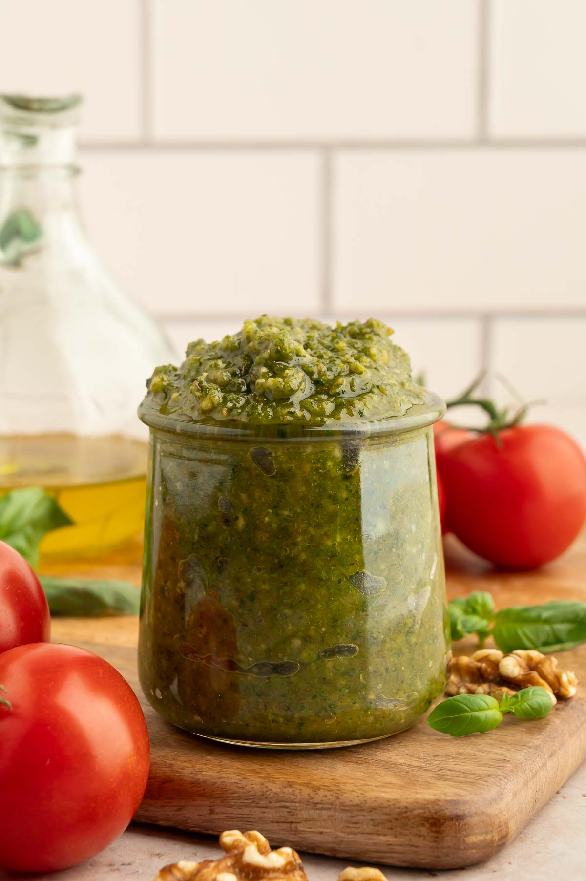 Walnut pesto sauce piled into a glass jar sitting on a wooden cutting board.