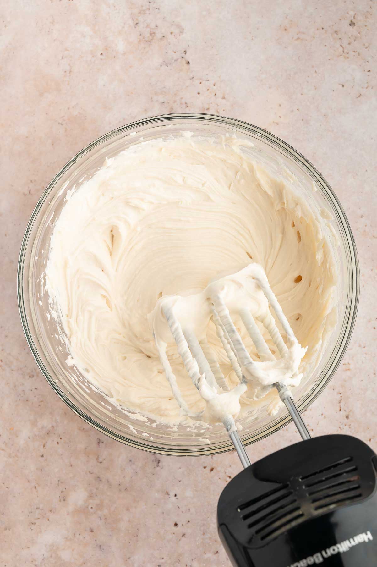 Vegan cream cheese and sugar whipped together in a bowl using an electric hand mixer.